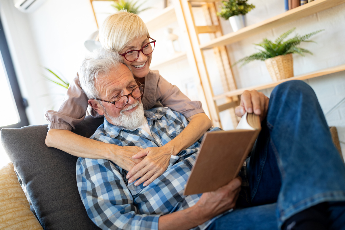 Beautiful old couple is reading a book and smiling at home