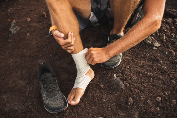 Man bandaging injured ankle. Injury leg while running outdoors.